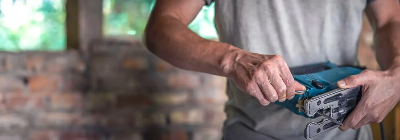 Elektrische Stichsäge mit einem Sägeblatt für Holz in den Händen eines Zimmermanns.